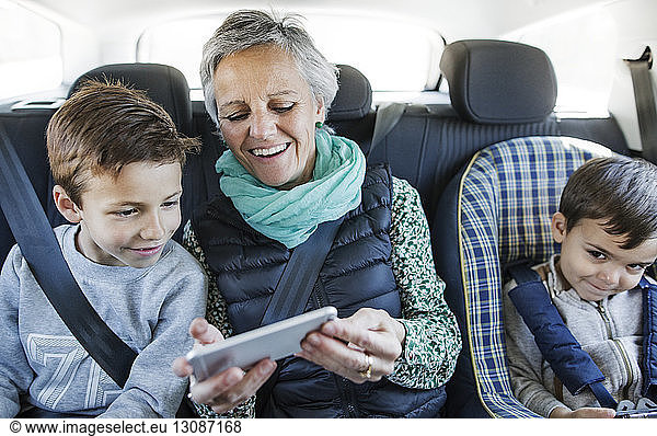 Happy senior woman using smart phone with grandsons in car