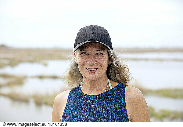 Happy senior woman wearing cap in front of lagoon