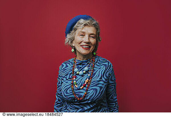 Happy senior woman wearing jewelry against red background