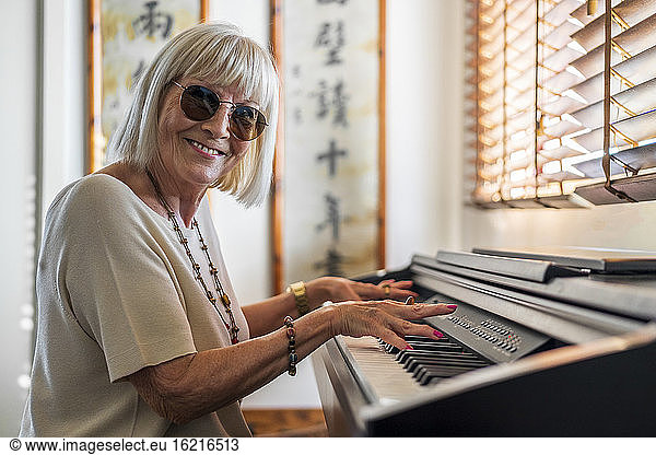 Happy senior woman wearing sunglasses playing piano at home
