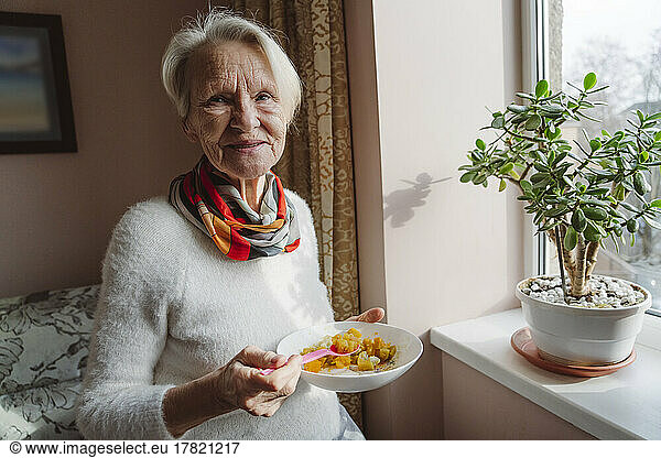 Happy senior woman with bowl by window