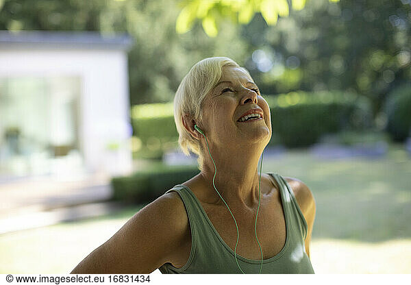 Happy senior woman with headphones exercising in summer garden