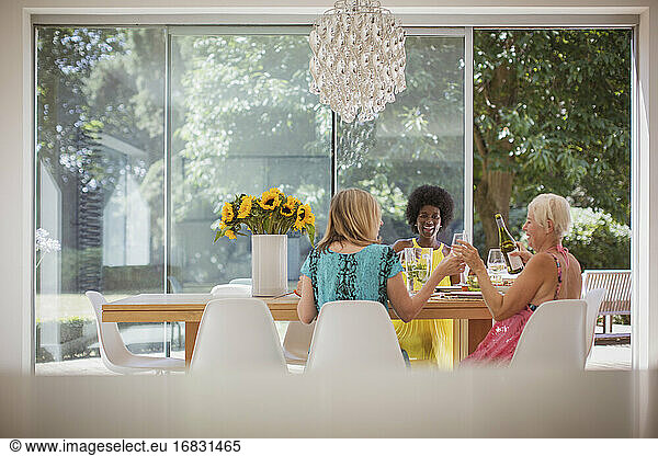 Happy senior women friends enjoying luncheon with wine at dining table