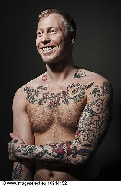 Happy shirtless tattooed man standing against black background