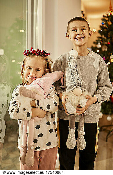 Happy sibling with toy gnomes standing in front of christmas tree at home