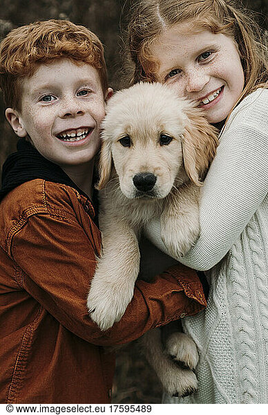 Happy siblings embracing golden retriever puppy