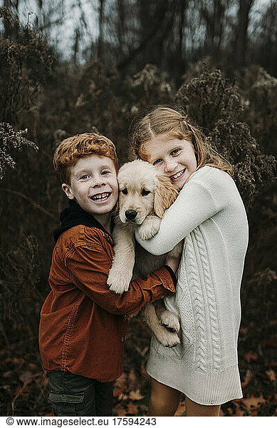 Happy siblings embracing golden retriever puppy in forest
