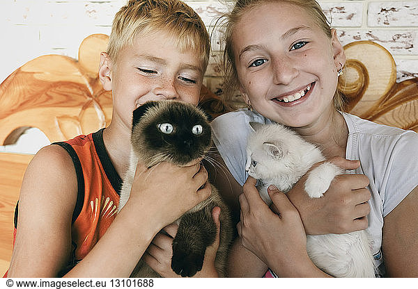 Happy siblings holding cats while sitting at home