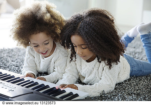 Happy sisters playing keyboard instrument on carpet at home