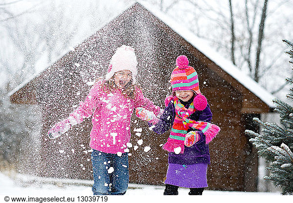 Happy sisters playing with snow during snowfall