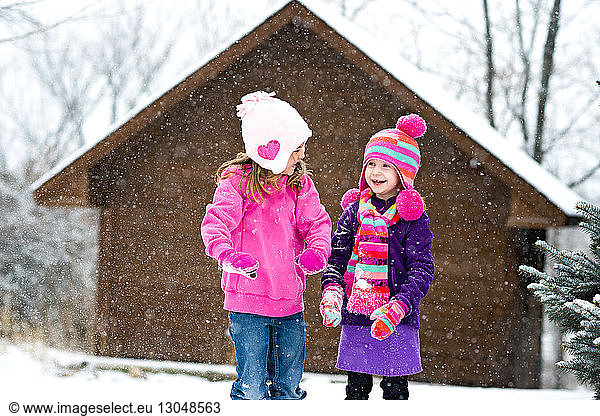 Happy sisters playing with snow while standing outdoors during snowfall