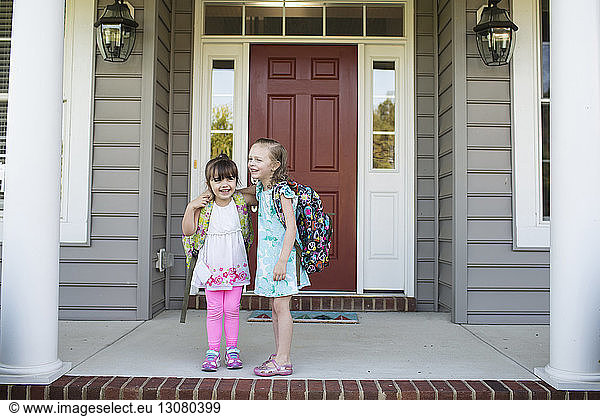 Happy sisters with backpack standing on porch