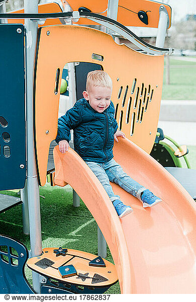 Happy Smiling Boy Going Down Slide on Cloudy Winter Day City