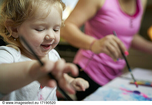 Happy smiling cute little girl painting with paintbrush