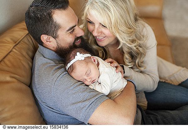 Happy smiling family holding newborn baby girl at home on couch