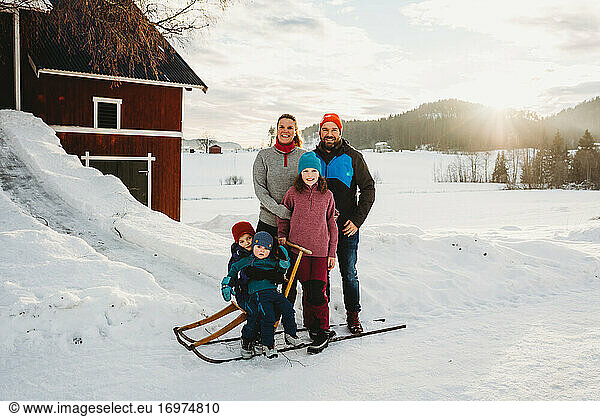 Happy smiling family in snowy countryside farm during sunset