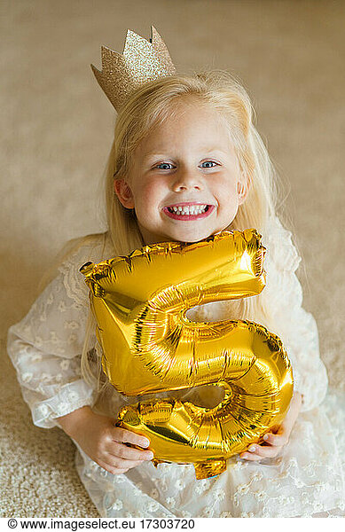 Happy smiling girl holding gold balloon number five.