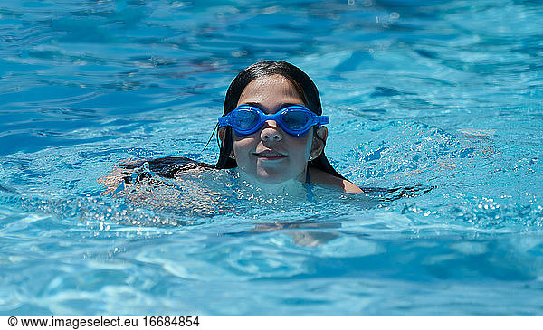 Happy smiling girl swimming and having fun in the pool with blue water