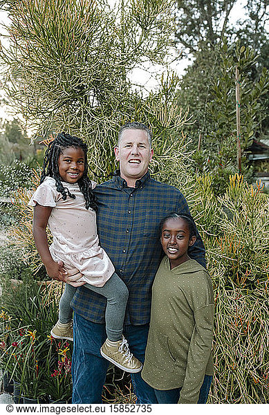 Happy smiling white dad holding black daughters outdoors