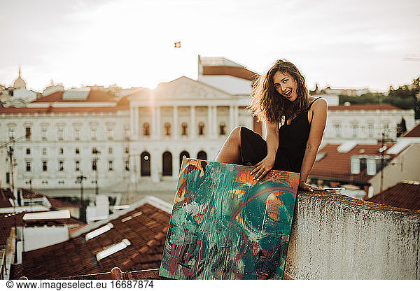 Happy smiling woman sitting on the roof holding abstract art painting