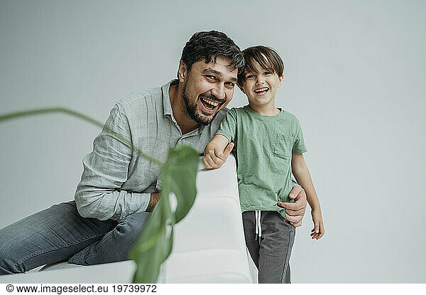 Happy son with father sitting on sofa against white background
