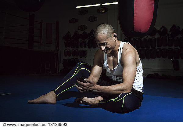 Happy sportsman using phone while sitting in gym