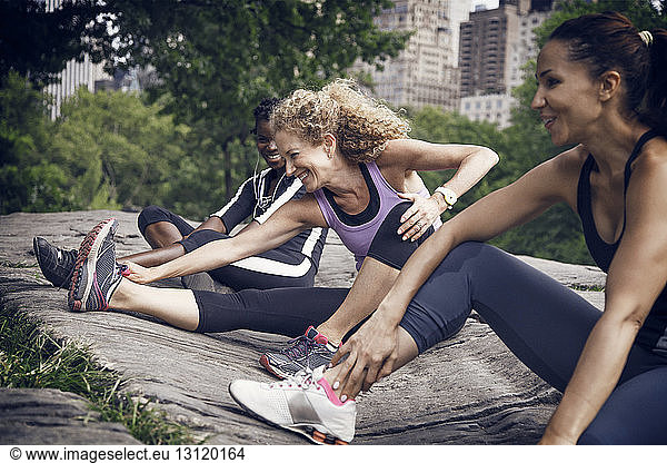 Happy sportswomen stretching on rock at park
