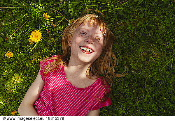 Happy strawberry blond girl lying on grass