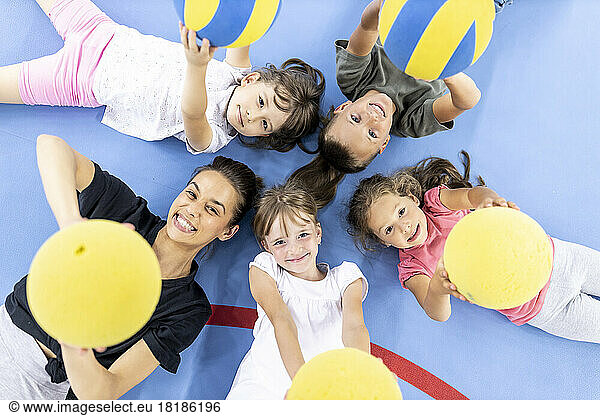 Happy students and teacher lying down with ball at school sports court