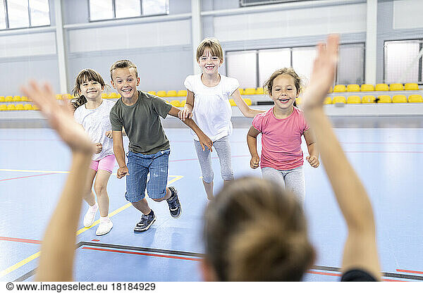 Happy students running towards teacher at school sports court