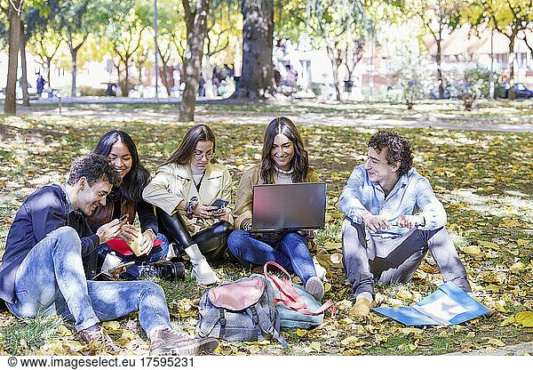 Happy students using smart phone and laptop in college park