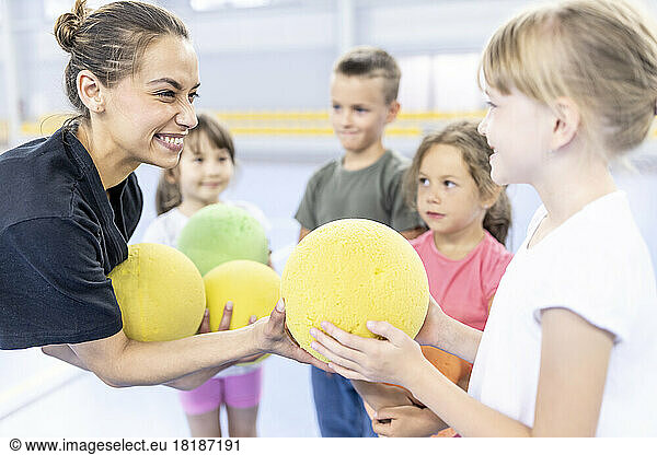 Happy teacher giving ball to student at school sports court
