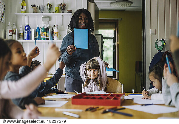 Happy teacher showing colored paper to students while teaching them in day care center