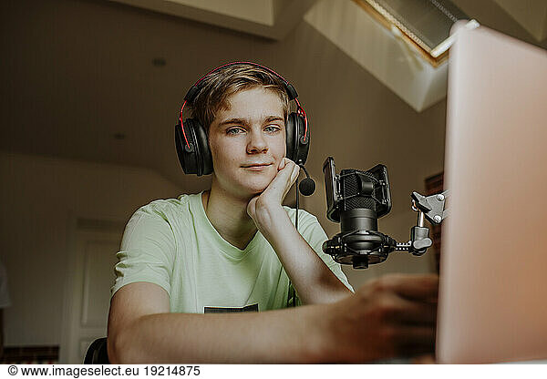 Happy teenage boy wearing headset and podcasting at home