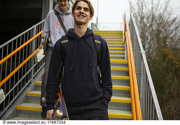 Happy teenage boy with skateboard descending urban stairs