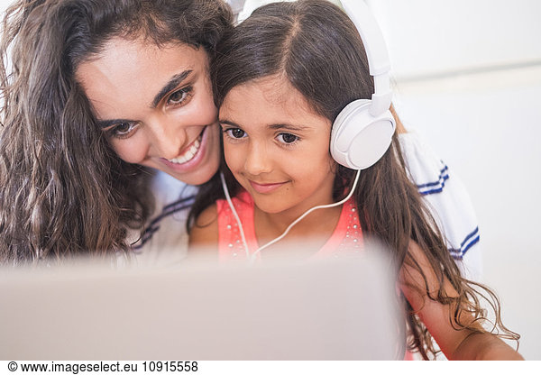 Happy teenage girl and her little sister with laptop and headphones