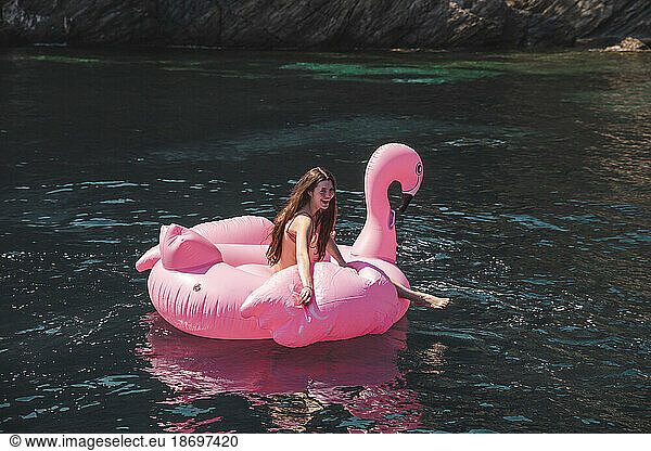Happy teenage girl floating on flamingo air mattress at vacation