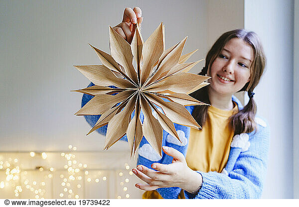 Happy teenage girl holding star shaped Christmas decoration at home