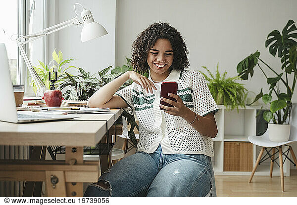 Happy teenage girl using mobile phone at desk