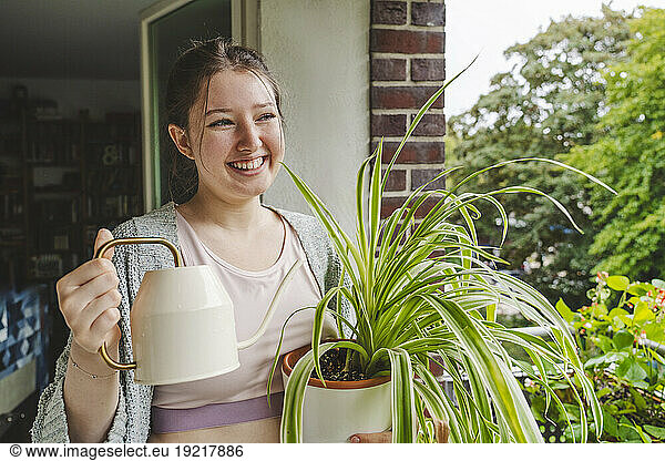 Happy teenage girl watering potted spider plant on balcony