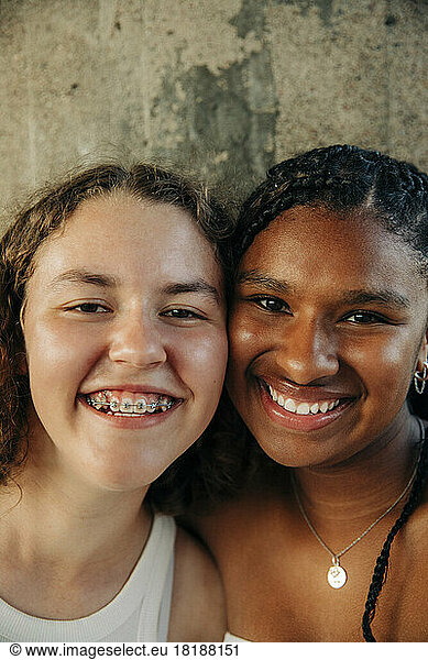Happy teenage girl wearing braces by female friend against wall