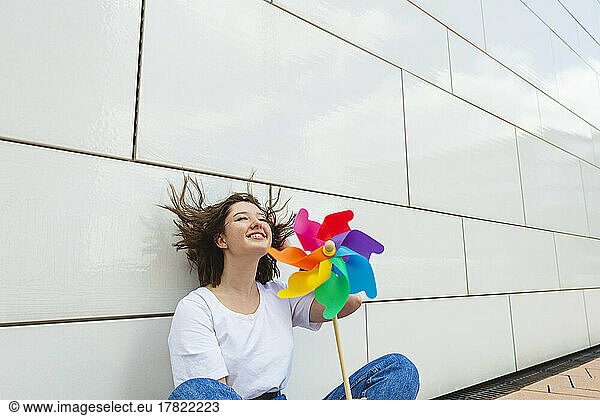 Happy teenage girl with multi colored pinwheel toy sitting in front of wall