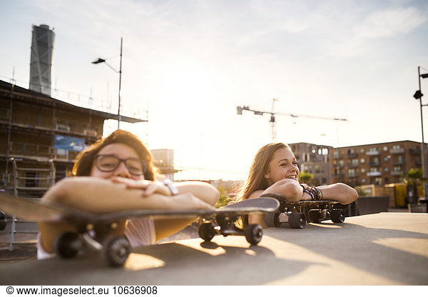 Happy teenage girls relaxing on skateboards at skate park
