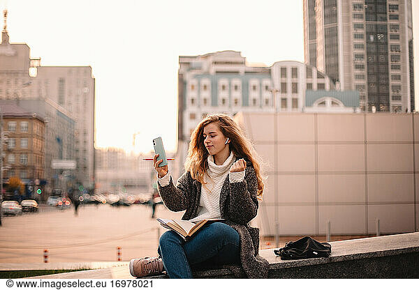 Happy teenage student girl doing video call using smart phone outdoors
