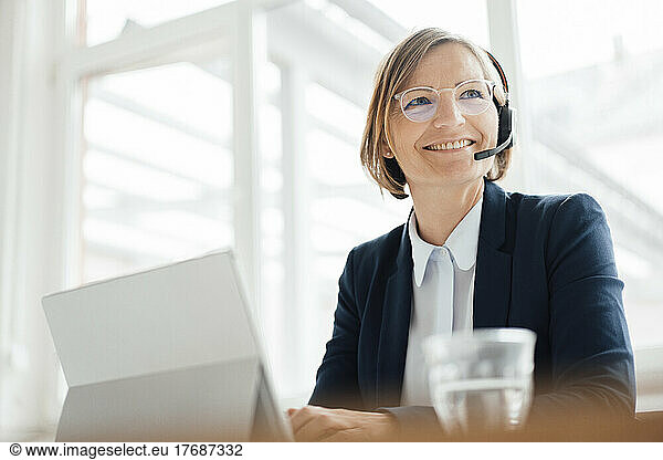 Happy telecaller wearing headset sitting with tablet PC in office