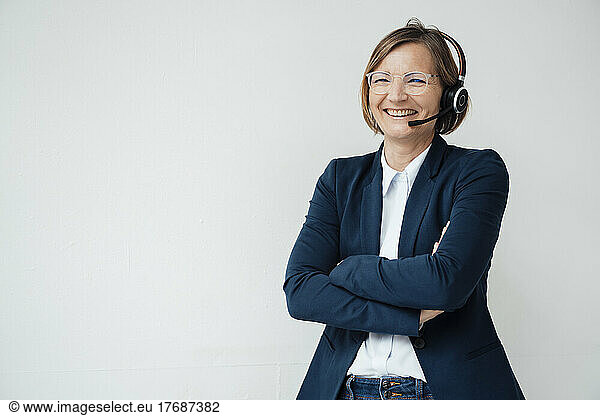 Happy telecaller wearing headset standing with arms crossed against white background