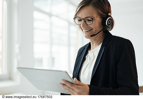 Happy telecaller wearing headset using tablet PC in office