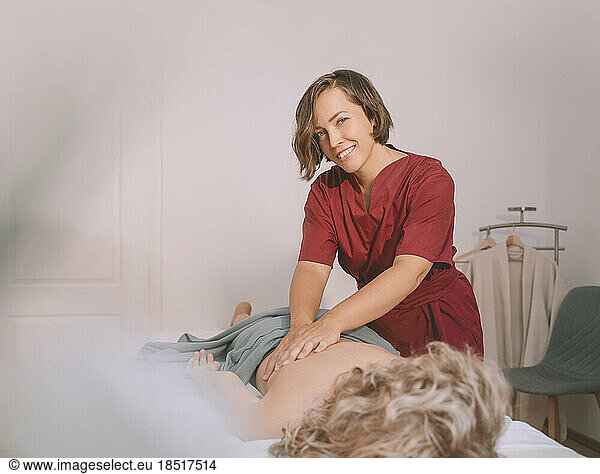 Happy therapist giving back massage to woman in spa