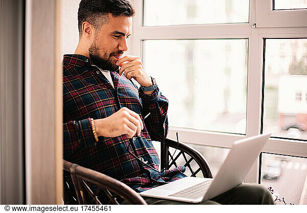 Happy thoughtful man using laptop computer at home