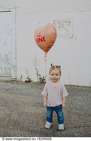 Happy toddler standing outside with heart valentines day balloon